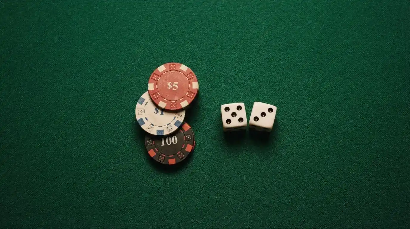 Vista cenital de fichas de casino y dados sobre una mesa de fieltro verde bajo luz suave.