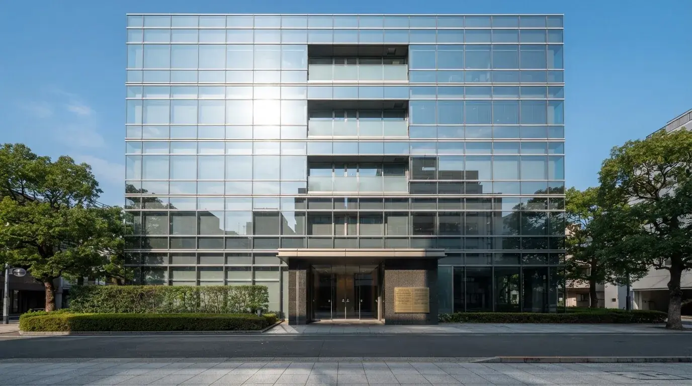 Un edificio de oficinas moderno con cristales reflectantes bajo un cielo despejado, visto desde una calle tranquila.