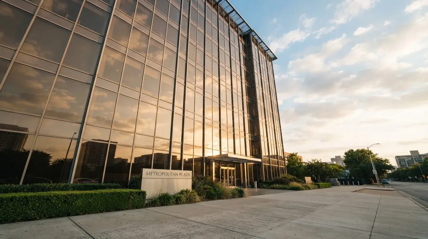 Un edificio de oficinas con fachada de cristal reflejando nubes, fotografiado desde una acera ancha por la tarde.